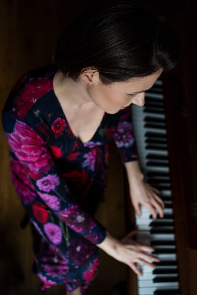 Top-down view of Aga looking at her hands placed on top of a piano keyboard. Aga is in a red-purple flower dress.